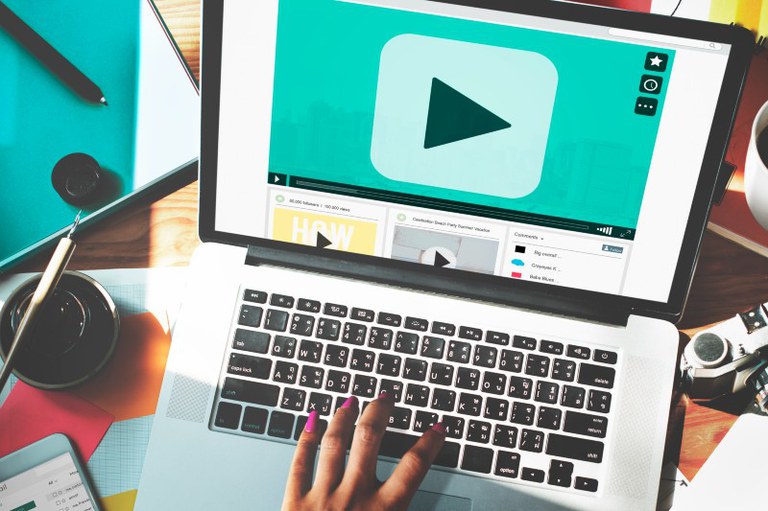 Imagem mostra uma mão feminina digitando manualmente no notebook com o botão de reprodução na tela