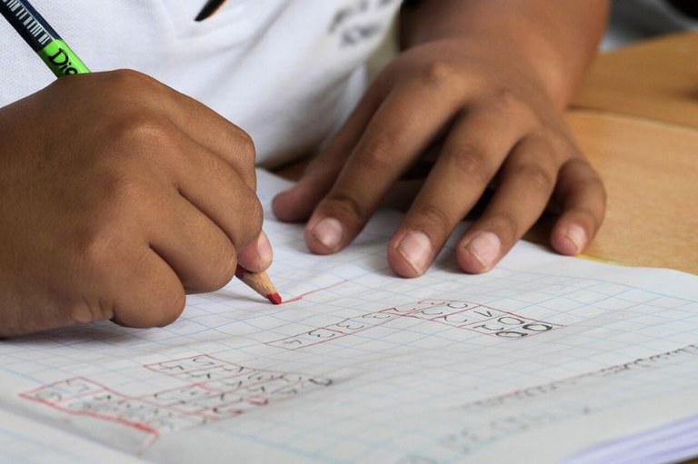 Foto em detalhe de uma criança com um lápis na mão escrevendo em um papel
