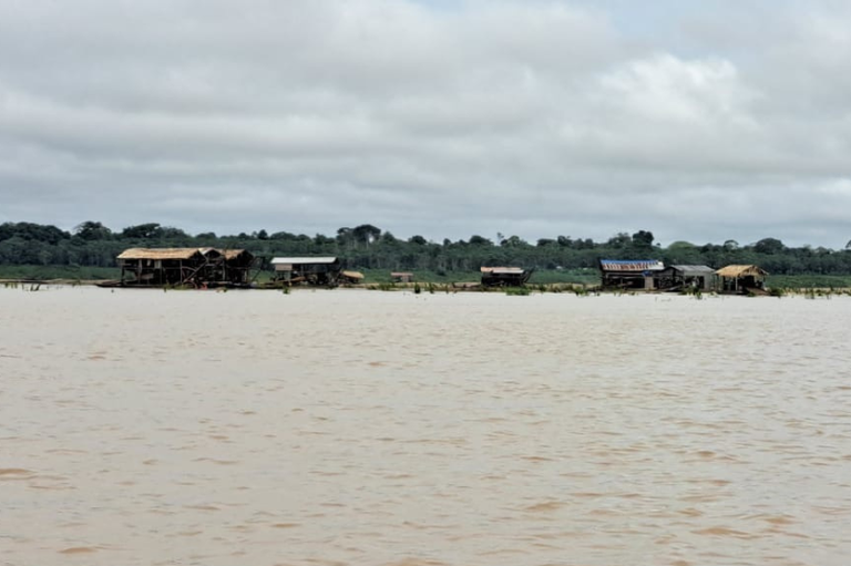 Foto do Rio Madeira tendo ao fundo, perto de uma das margens do rio, diversas balsas de garimpo