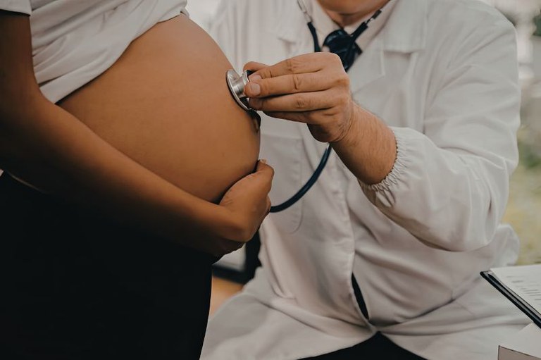 Foto mostra em detalhe um  médico examinando com estetoscópio a barriga de uma gestante