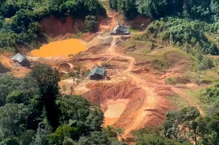 Vista aérea de área desmatada no meio da floresta com solo exposto alaranjado, pequenos tanques de água barrenta e estruturas improvisadas, evidenciando atividade de garimpo.