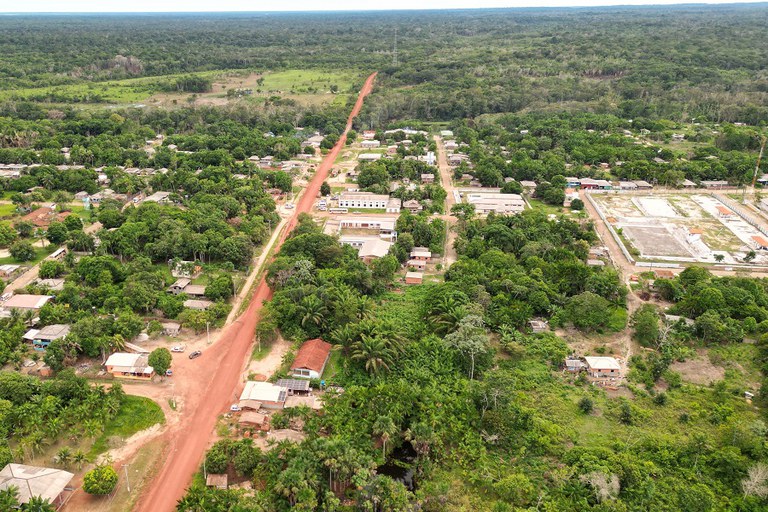 Imagem aérea do assentamento agroextrativista Maracá. Uma estrada de terra corta ao meio a floresta em que há várias árvores, casas e outros imóveis