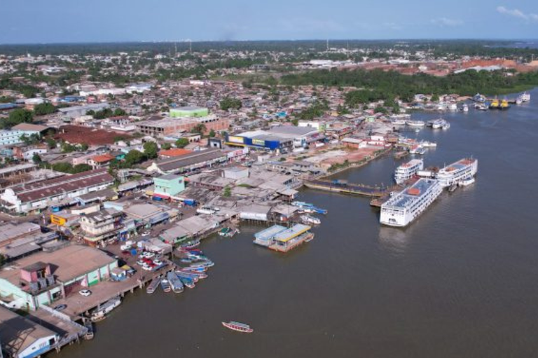 Foto da vista aérea da região portuária de Santana, que mostra parte do rio e barcos atracados na margem, com construções e casas ao redor.