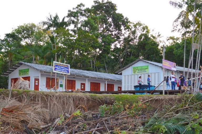 Estudantes caminham em passarela de madeira em frente à Escola Bosque, que tem árvores e palmeiras ao fundo