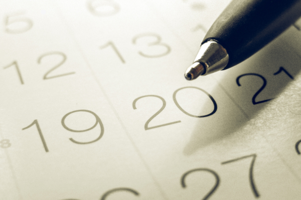 Caneta sobre folha do calendário ampliada apontando para os dias 19 e 20