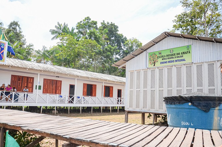 Fachada da Escola Bosque construída em madeira. Há alguns alunos pelo corredor