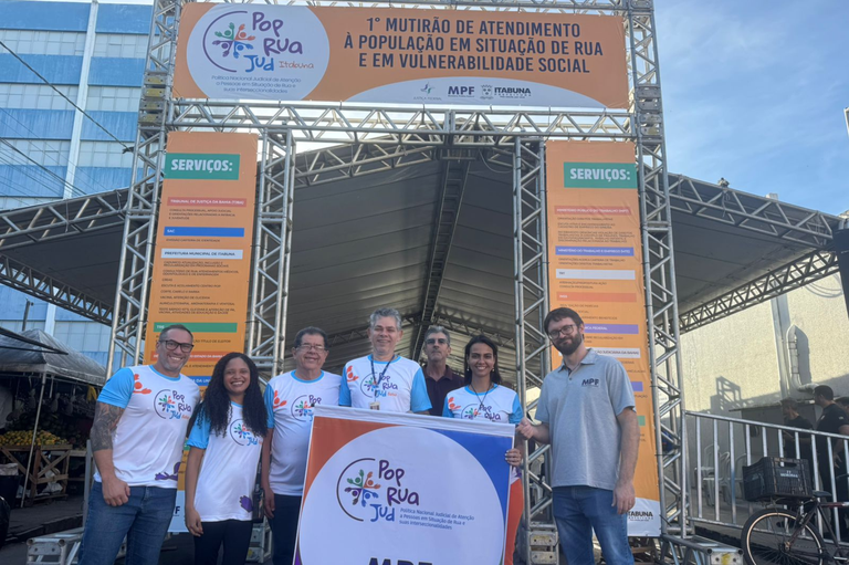 Equipe do MPF em frente ao Mutirão Pop Rua Jud em Itabuna, segurando banner do evento.