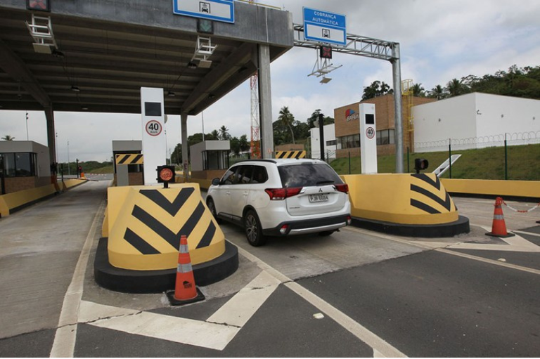 Foto mostra estrutura de pedágio na Via Metropolitana, vê-se um carro branco próximo do guichê de pagamento do pedágio