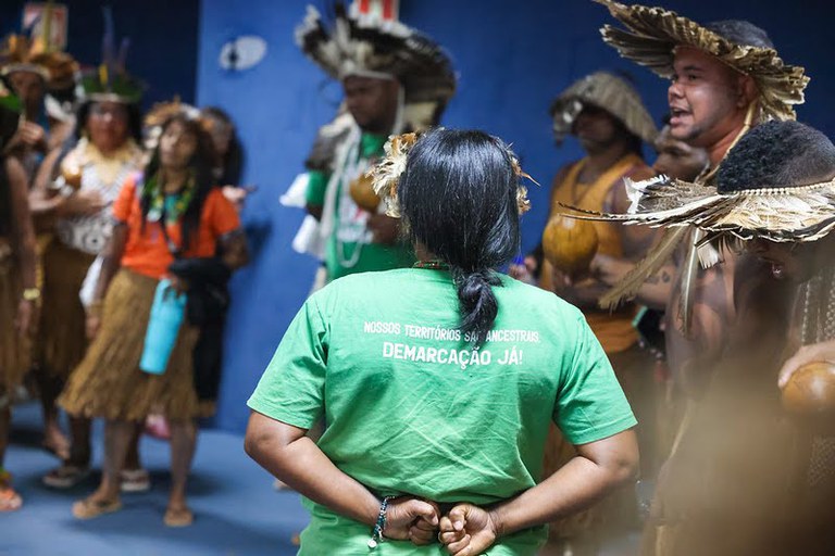 Uma imagem de um grupo de pessoas de uma tribo indígena, reunidas em uma sala.
