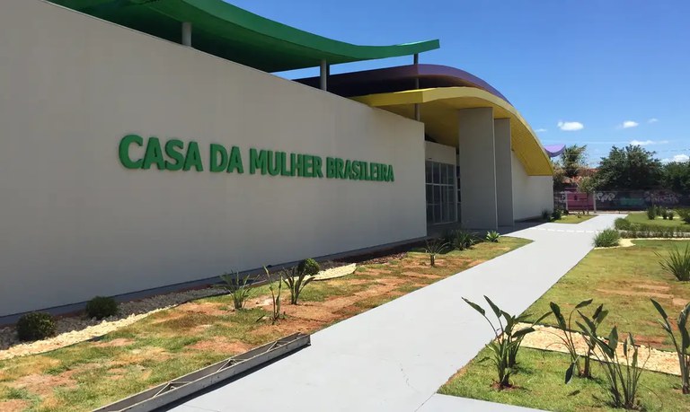 A foto ilustrativa mostra a fachada de uma Casa da Mulher Brasileira, com as letras em verde sobre parede branca.