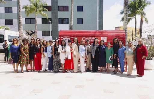 Inauguração do Banco Vermelho na sede da Defensoria Pública da Bahia. Autoridades mulheres estão reunidas em frente ao banco para chamar a atenção da sociedade para a urgência do combate à violência de gênero.