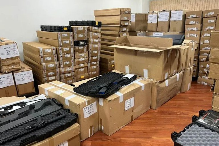 Foto mostra caixas de armas apreendidas empilhadas. Duas delas estão abertas e mostram os fuzis