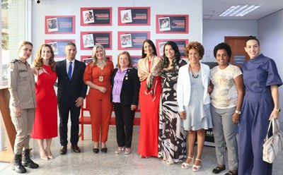 MPF Foto de grupo com 10 pessoas em frente aos painéis da campanha Banco Vermelho. As pessoas estão lado a lado, em pé, no hall da sede do MPF/BA. Ao fundo, aparecem os relatos que integram a campanha, dispostos em painéis vermelhos e pretos. A imagem registra as autoridades mulheres presentes na solenidade de inauguração da campanha, acompanhadas do procurador-chefe Claytton Santos.