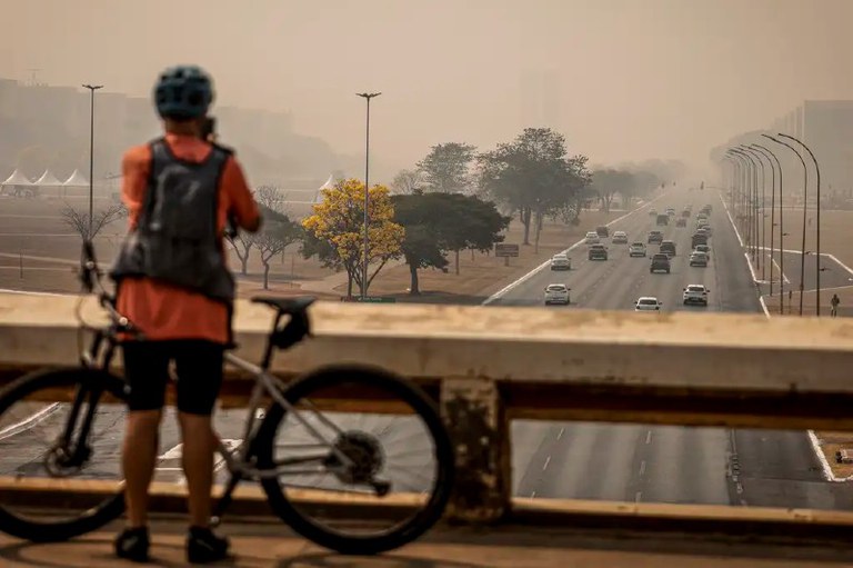 Imagem mostra um ciclista olhando o céu com fumaça na Esplanada dos Ministérios, em Brasília