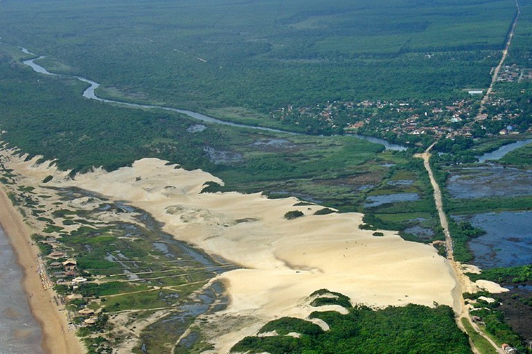 Foto aérea mostra parque com vegetação e dunas de areia. Casas e loteamentos circundam o parque