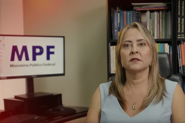 A imagem mostra uma mulher sentada em uma cadeira de escritório, com uma estante de livros ao fundo. No canto esquerdo da imagem, há um computador exibindo a logo do MPF