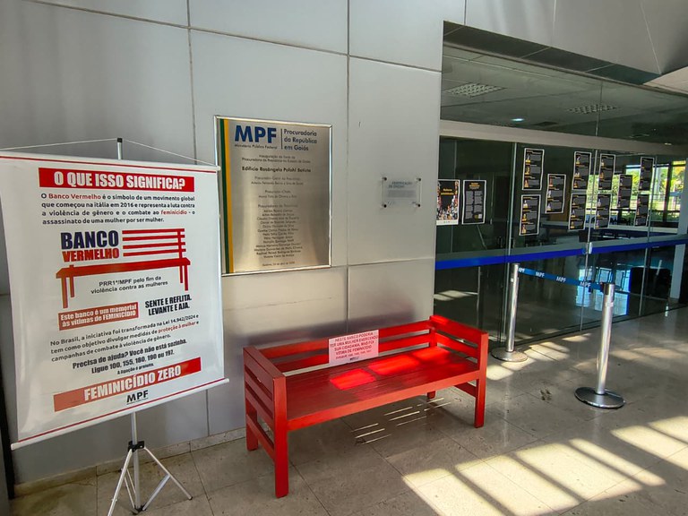 A imagem mostra uma exposição de conscientização no hall de entrada da Procuradoria da República em Goiás (MPF), focada no combate à violência contra a mulher e ao feminicídio.