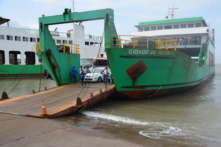 Foto de ferryboat verde e branco "Cidade de Tutóia I" com a rampa baixada, contendo veículos e pessoas em seu interior em uma área de embarque.