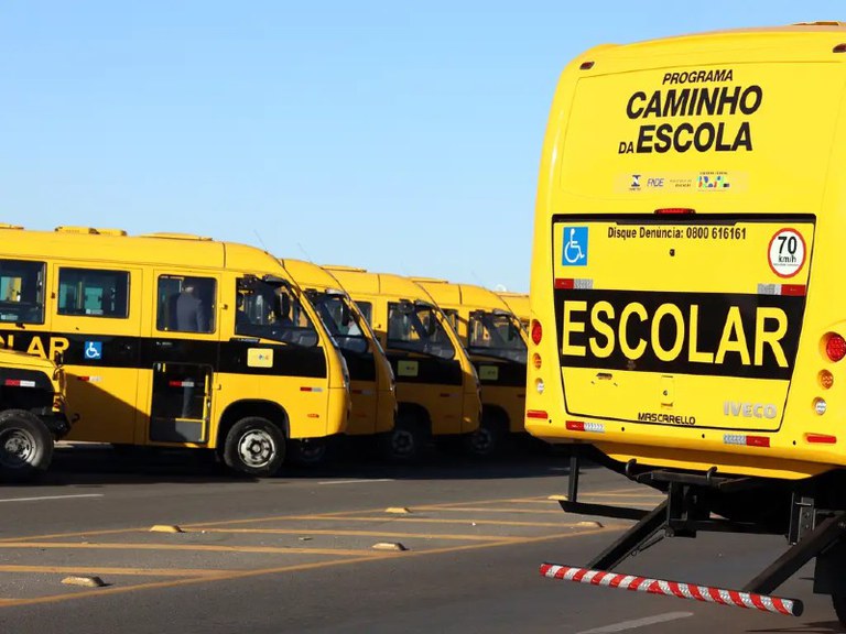 Foto de ônibus escolar amarelo. No fundo do veículo está escrito Caminho para a Escola
