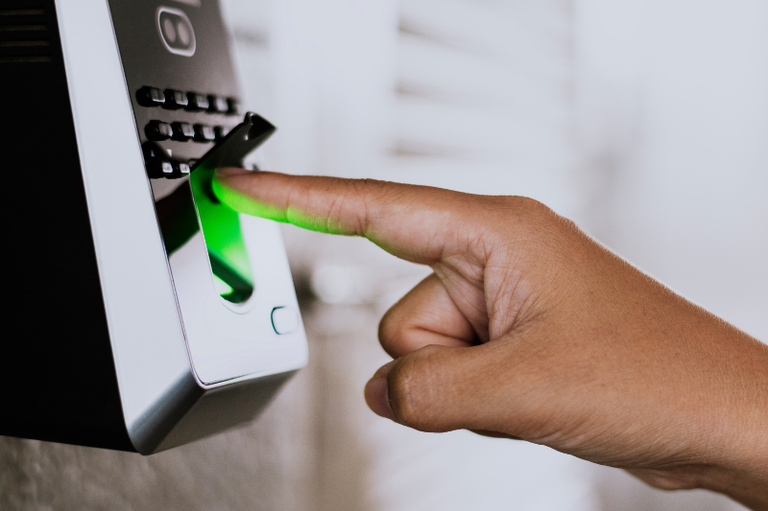 Foto mostra detalhe de mão com o dedo indicador em um relógio de ponto digital/biométrico