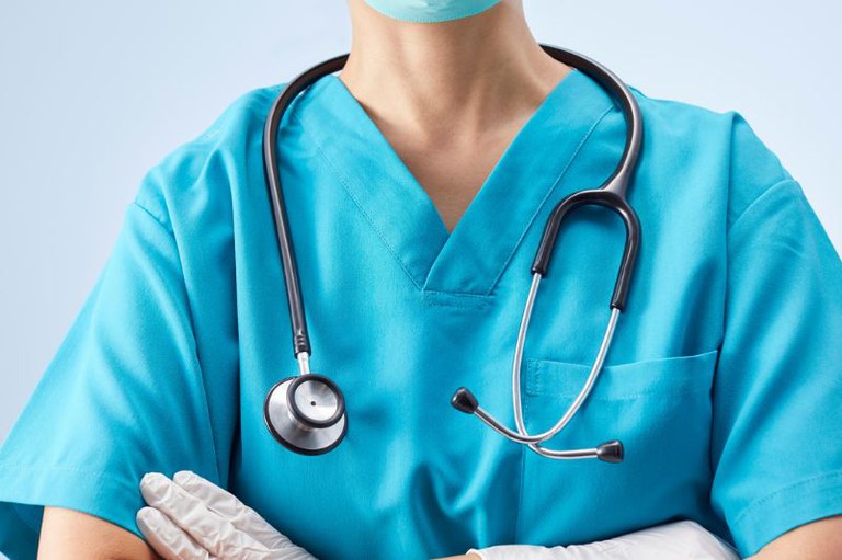 foto mostra em detalhe um médico com braços cruzados e usando roupas de hospital com um estetoscópio pendurado no pescoço