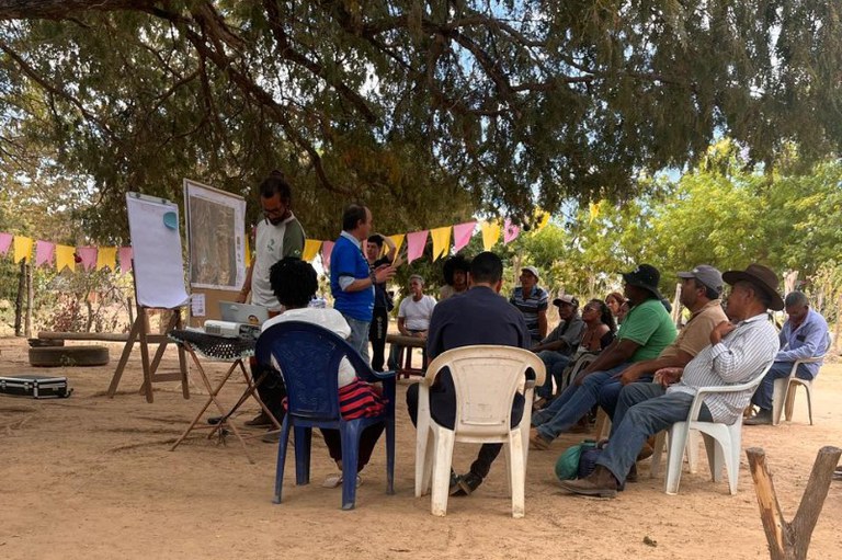 Foto mostra comunidade reunida embaixo de uma árvore. O procurador Edmundo está em pé conversando com eles