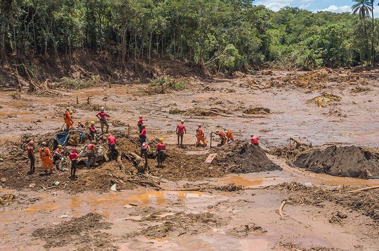 Foto mostra destruição causado pelo rompimento da barragem. Bombeiros tentam resgatar vítimas
