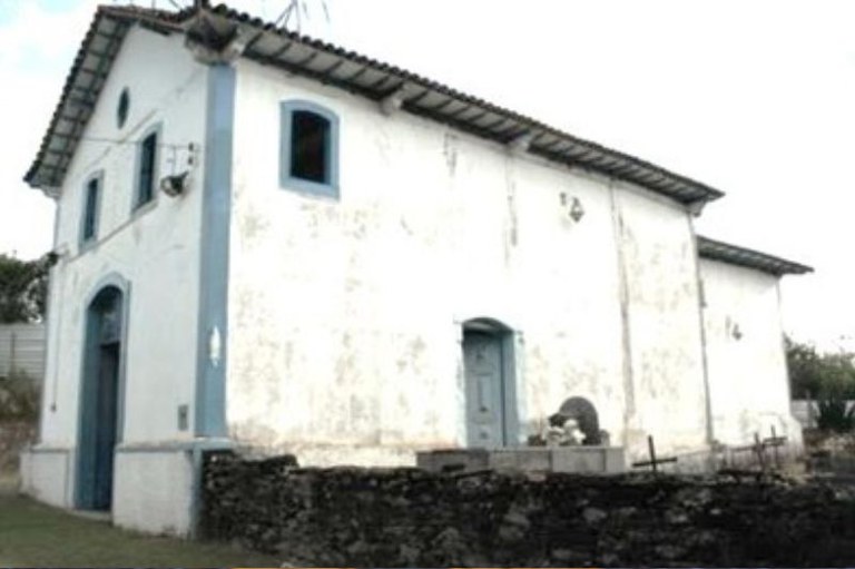 Foto da Capela de Nossa Senhora das Mercês mostra a lateral branca e um muro de pedras
