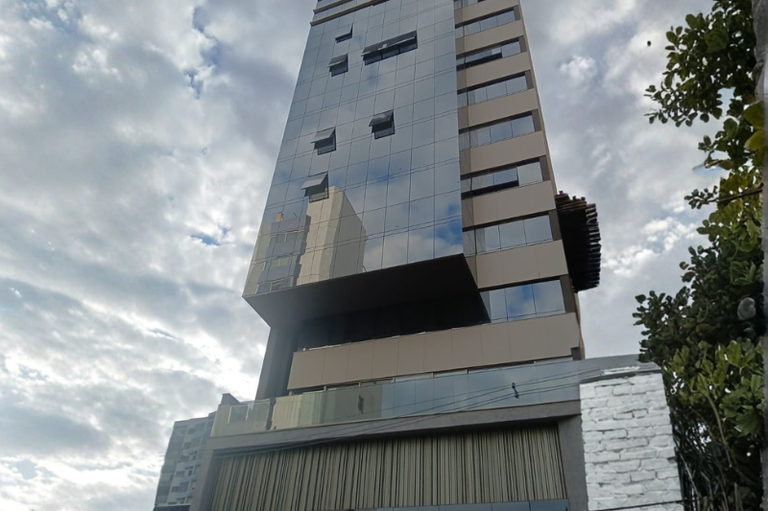 Foto mostra a fachada da unidade. Um prédio alto espelhado