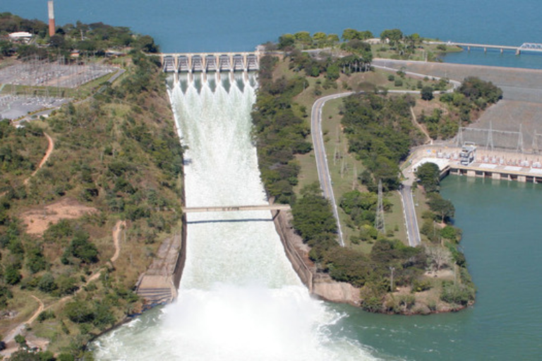 foto mostra vista aérea da usina, mostrando a barragem ao fundo e as comportas liberando água para o curso do rio