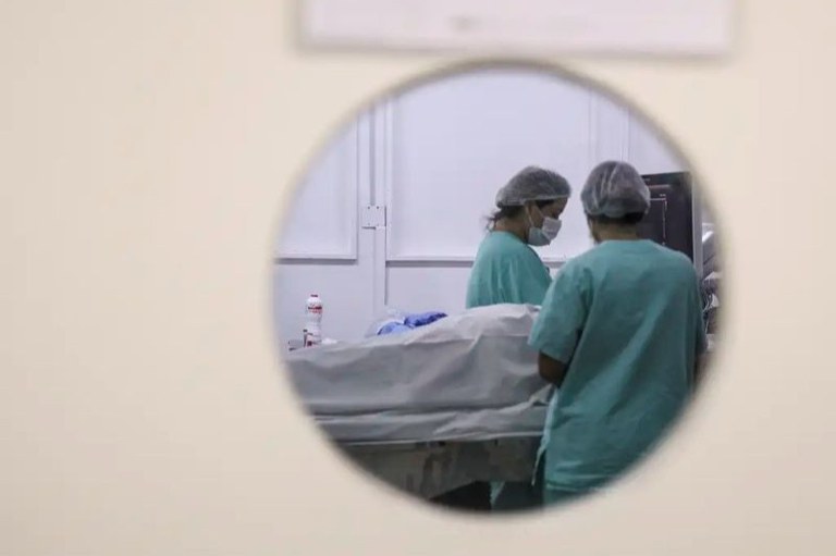 Foto em que se vê um paciente por trás de uma porta que possui uma janela redonda de vidro.