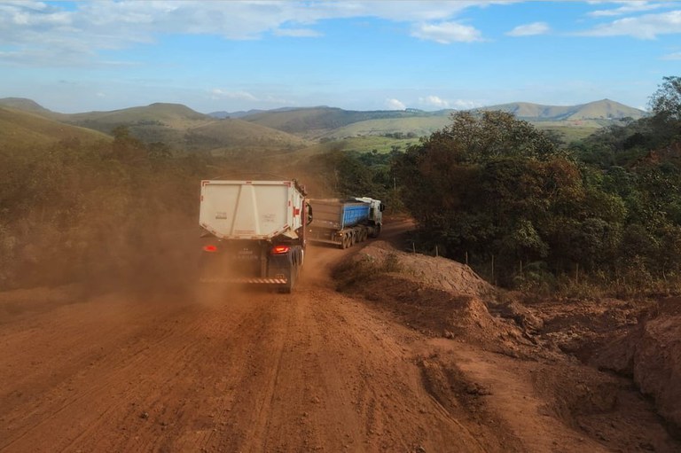 Fotografia das trazeiras de dois caminhões em uma estrada de terra, levantando poeira