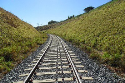 Imagem mostra trecho de uma linha de trem de ferro no meio de um vale.