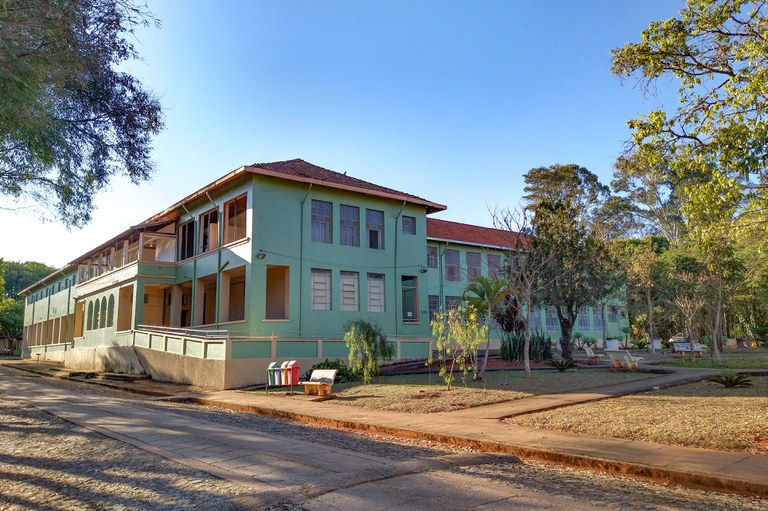 Fotografia da fachada da Casa de Saúde São Francisco de Assis, em Bambuí (MG). O hospital está em perspectiva, tem dois pavimentos, pintado da cor verde claro e com uma rua à frente e árvores ao redor.