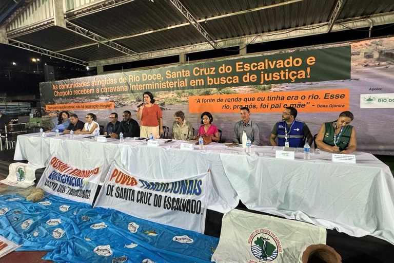 Fotografia dos representantes dos órgãos públicos presentes no evento sobre o Acordo de Repactuação de Mariana, sendo 11 pessoas, das quais 10 sentadas na mesa do evento, entre os quais o procurador da República Eduardo Henrique de Almeida Aguiar, além de uma mulher em pé, falando ao microfone. Todos estão em um ginásio esportivo, com o banner do evento atrás da mesa e faixas na frente da mesma.