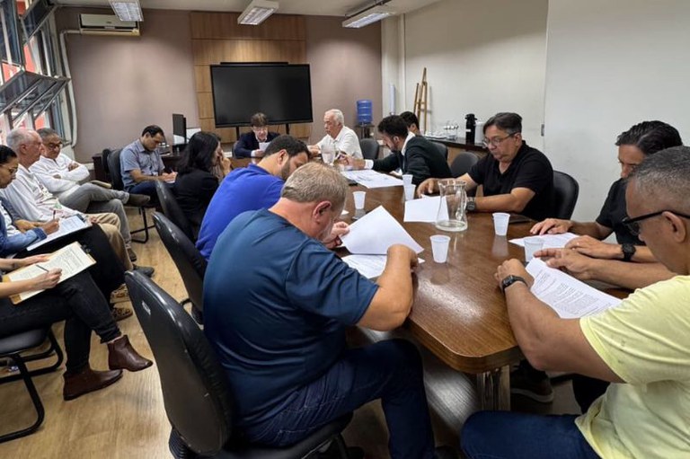 Foto mostra participantes da reunião sentados ao redor de uma mesa oval