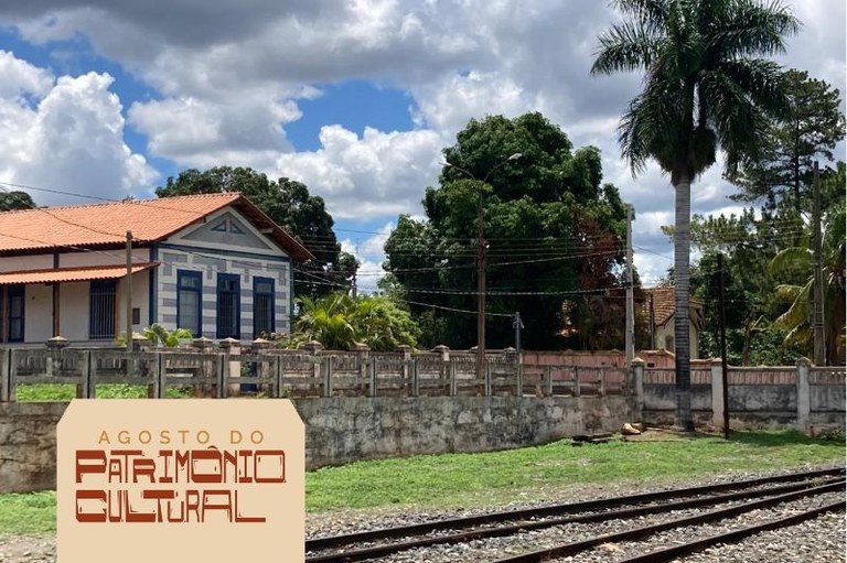 Foto mostra o complexo ferroviário de Corinto com uma construção em alvenaria e uma linha de trem na frente