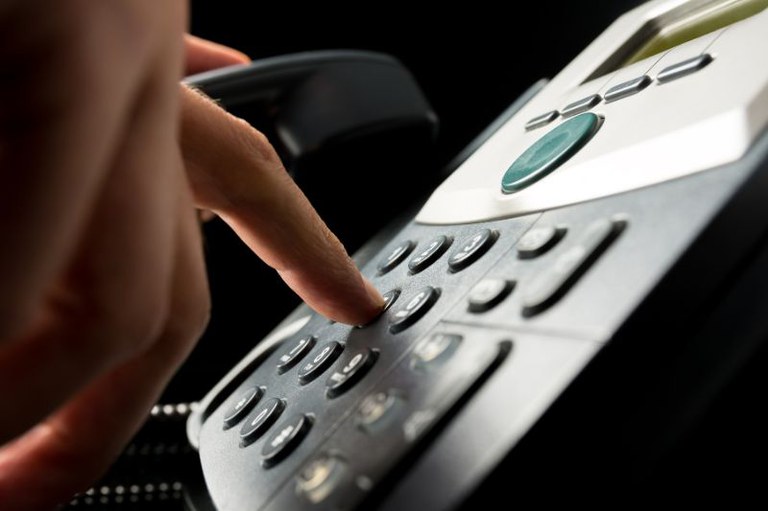 Foto mostra em detalhe uma pessoa apertando a tecla de um telefone preto