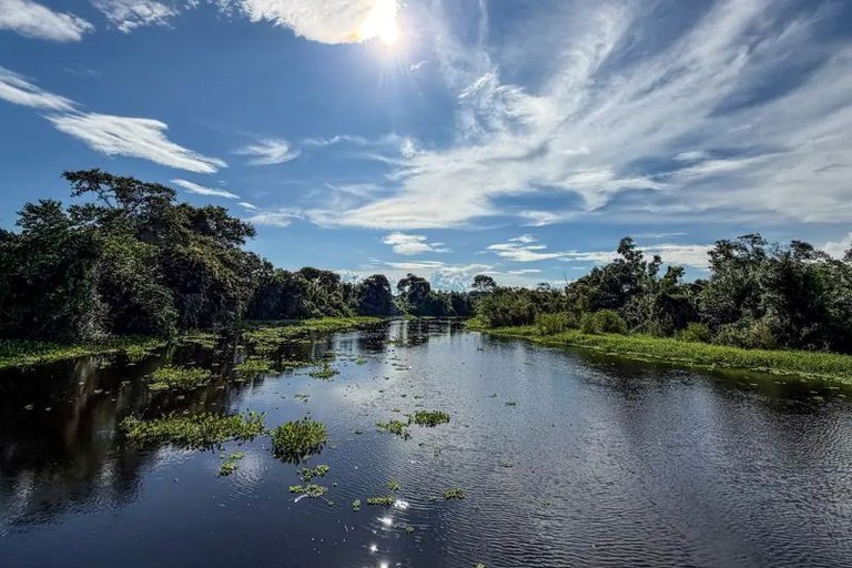 Foto da Fazenda San Francisco, em Miranda (Pantanal Sul). É possível ver um grande rio, as margens são cobertas por árvores altas e folhagens densas e preservadas. O dia está bonito, com céu azul e nuvens escondendo o Sol. A fazenda faz parte da Bacia do Alto Paraguai.