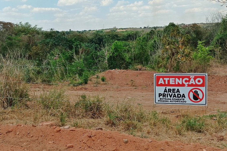 Foto mostra um local de mata com espaços desmatados. Na cerca há um aviso de área privada