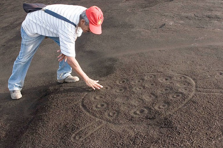 Foto mostra homem abaixado analisando marcas em uma pedra