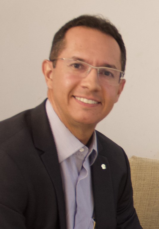 homem de terno azul escuro e camisa branca sentado de lado sorrindo