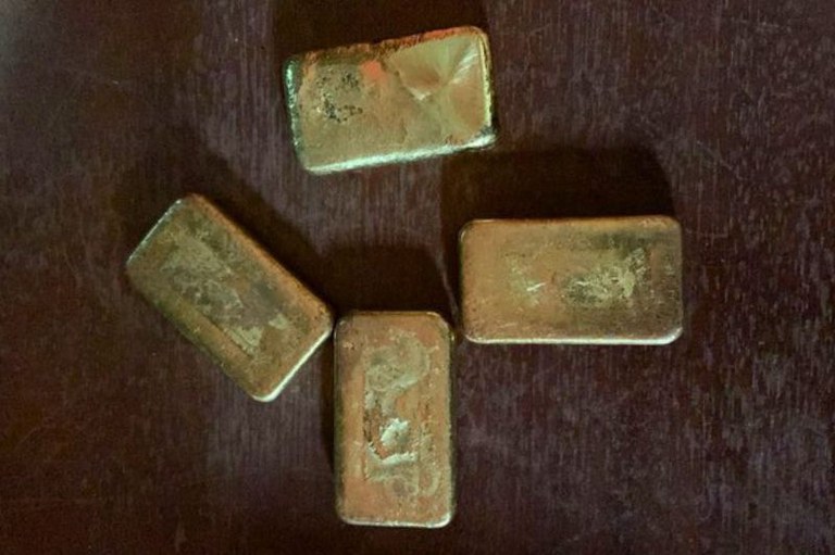 A imagem mostra quatro barras de ouro em uma superfície de madeira escura.