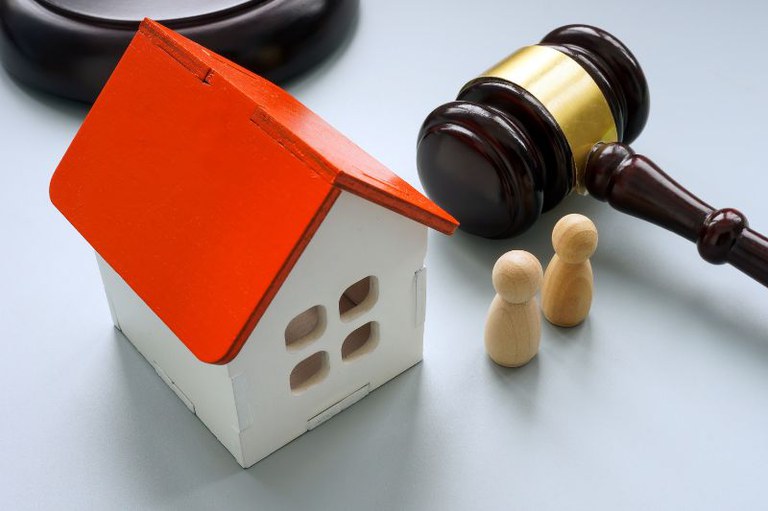 Foto de um martelo de juiz ao lado de uma casa em miniatura e duas figuras humanas de madeira.