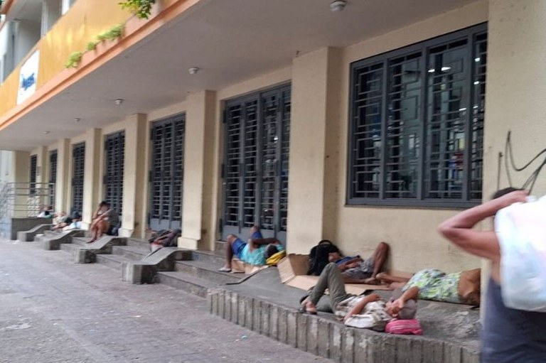 Pessoas deitadas nas escadarias da sede dos Correios em Belém. O prédio tem diversas portas e janelas de metal.
