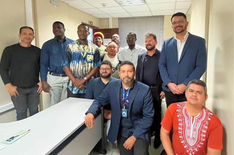 Um grupo de doze homens, em pé e sentados, posa para uma foto em um ambiente de escritório, com uma mesa branca à frente.