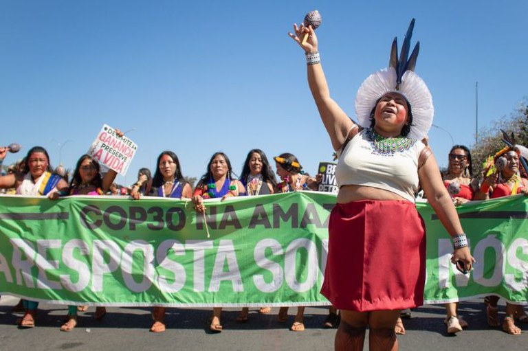 Mulheres indígenas marcham na rua segurando faixa verde escrita COP30 na Amazônia - A Resposta Somos Nós.