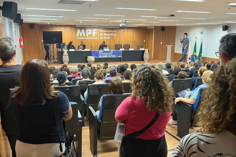 Vista de auditório lotado, de costas para a câmera, com painel ao fundo: "MPF - Ministério Público Federal - Procuradoria da República no Pará" e faixa "Escuta Pública - Privatização da Saúde no Pará" com pessoas sentadas e outras no palco e púlpito.
