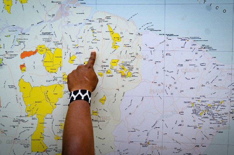 Foto em plano médio foca no braço e mão de uma pessoa de pele retinta que aponta para a Terra Indígena Amanayé em um mapa do Brasil com áreas amarelas.