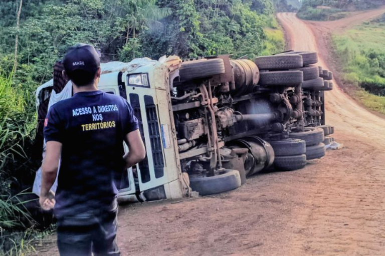 Um homem de costas observa um caminhão acidentado, tombado em um trecho de terra da rodovia Transamazônica, em área cercada por vegetação densa.
